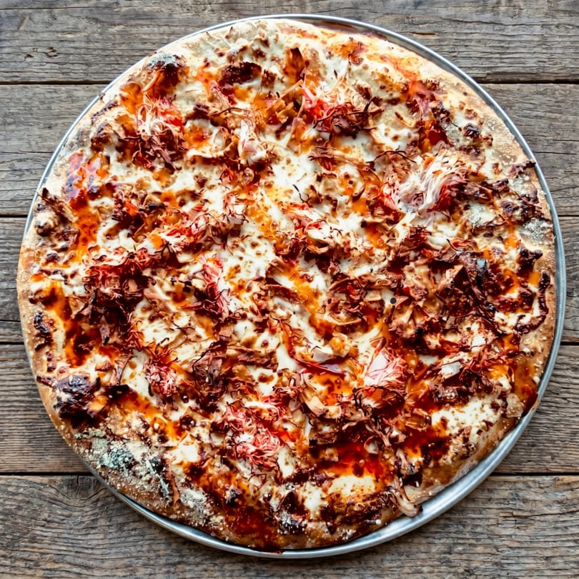 A whole pizza with white cheese, red sauce, and shredded meat on a wooden table.