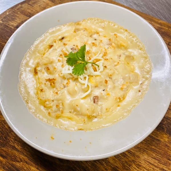 Creamy baked macaroni and cheese, topped with shredded cheese and a sprig of cilantro, on a white plate.