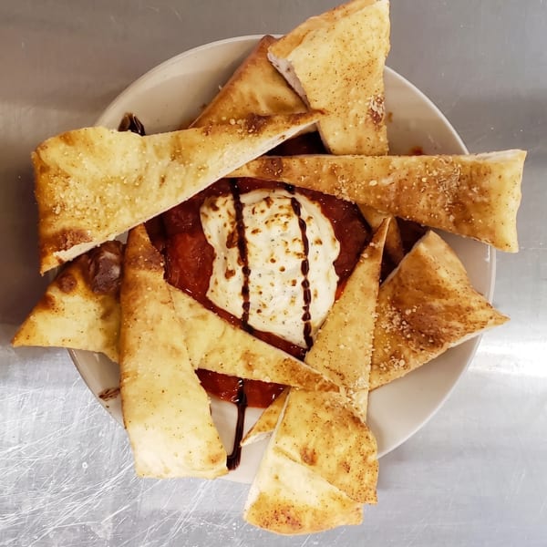 A plate of toasted pita bread triangles surrounding a dollop of cheese and red sauce.