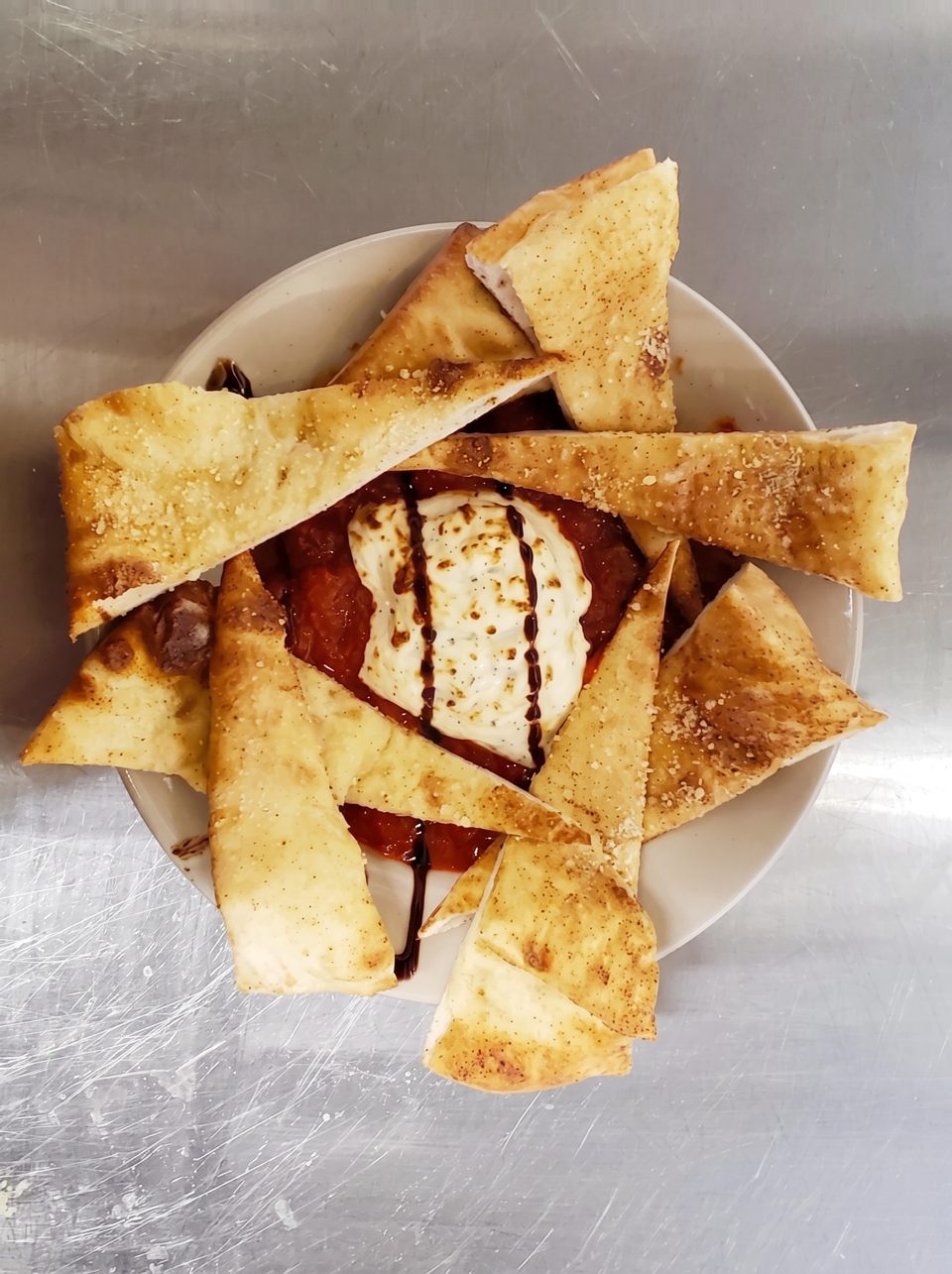 A plate of toasted pita bread triangles surrounding a dollop of cheese and red sauce.