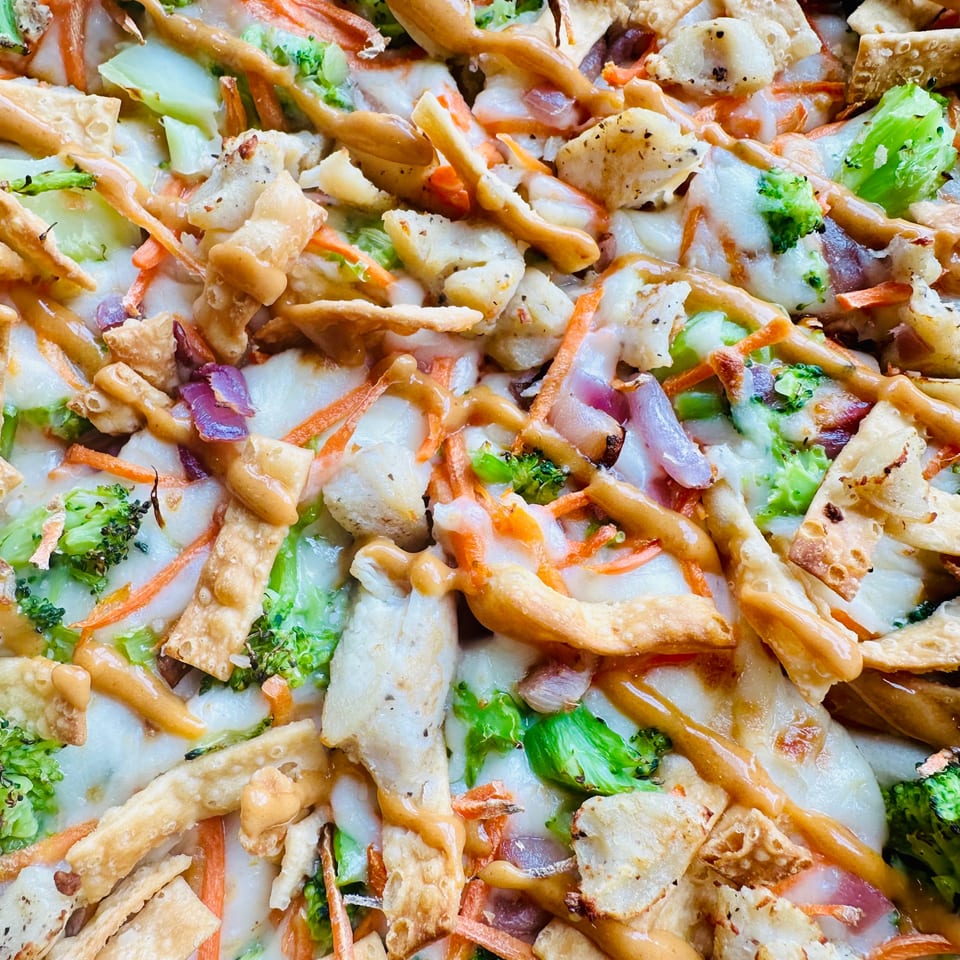 Close-up of crispy vegetable stir-fry with broccoli, carrots, onions, fried noodles, and creamy sauce.