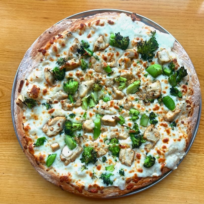 White pizza with chicken and broccoli on a wooden table.